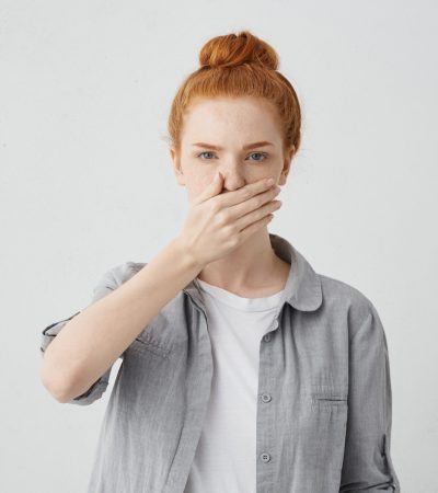 indoor-shot-serious-young-caucasian-woman-with-ginger-hair-wearing-casual-clothing-covering-mouth-with-hand-as-sign-keeping-secret-some-confidential-information-feeling-frustrated